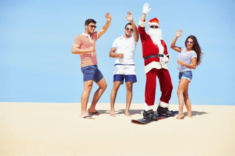 3 people standing on a sand dune in shorts and t-shirts with santa in the middle getting ready to sand board