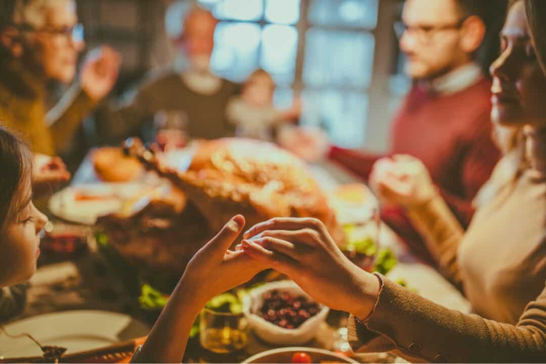 A family praying over a thanksgiving meal with a large turkey dinner in the middle