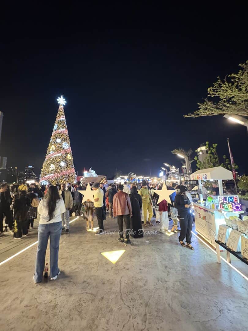 Entrance to the Christmas market area with lots of people standing on the pathway and the lit up Christmas tree further in the background