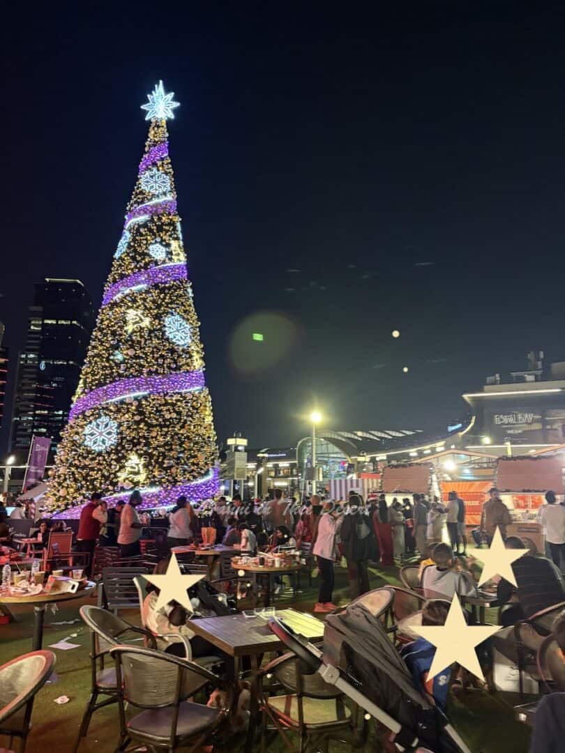 Seating area for eating food from the food trucks close to the large lit up Christmas tree with lots of people sat in the area