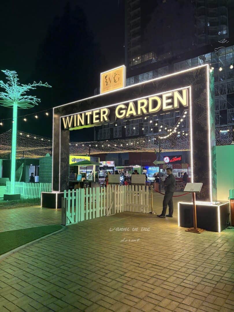 Entrance to Winter Garden at Al Habtoor City, with lit up green electric palm trees and a white wodden gated entry plus neon sign