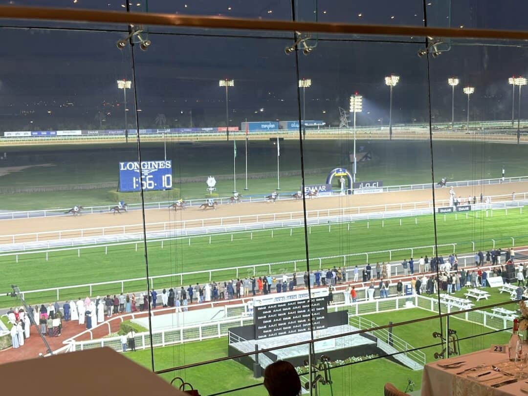 Horses racing to the finish line at Meydan Racecourse with a view from the hospitality area of Meydan