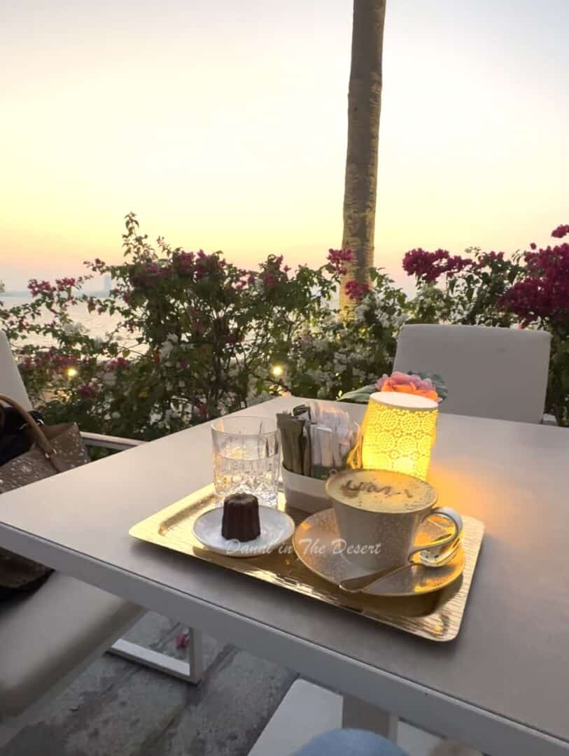 Gold cappucino and a small cake, set on a gold tray on a table at UMA lounge overlooking the Arabian Sea