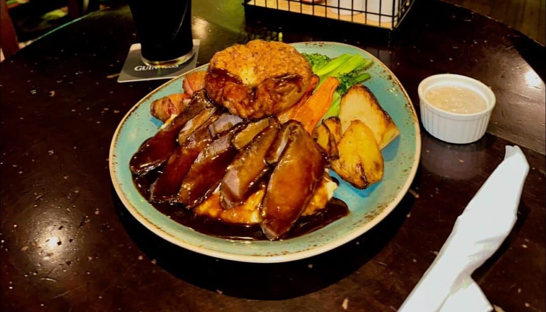 A traditional Sunday roast with beef, potatoes, carrots and broccoli served with gravy over the food and horseradish sauce on the side