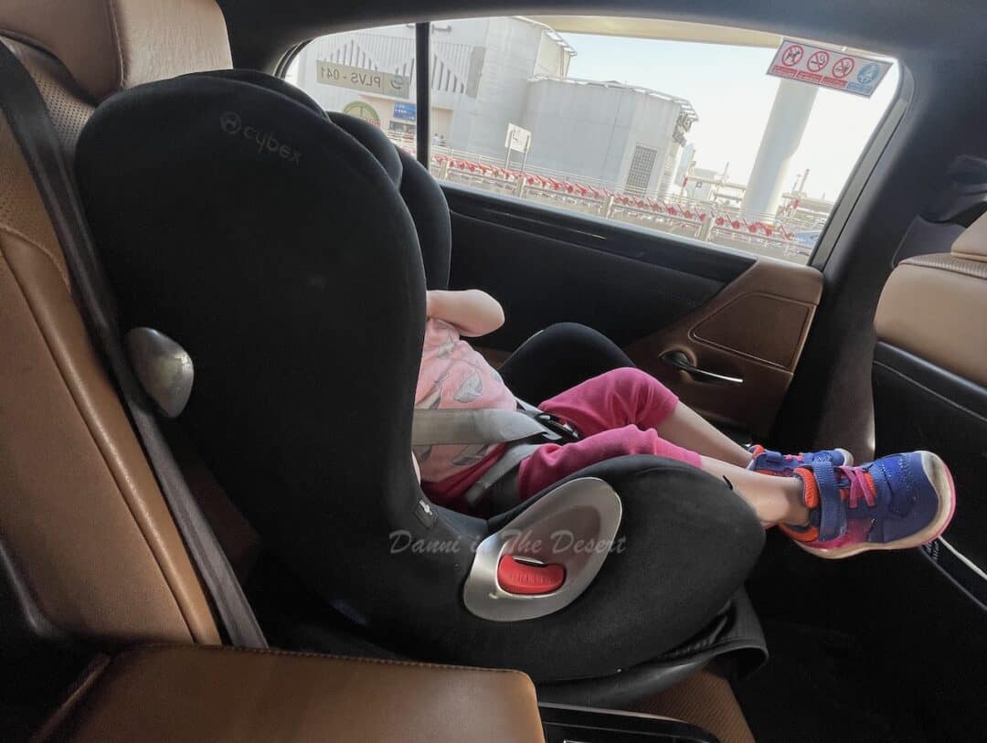 Toddler with pink leggings and blue trainers sat in a black Cybex forward facing car seat in a Careem Lexus taxi with brown leather chairs in Dubai