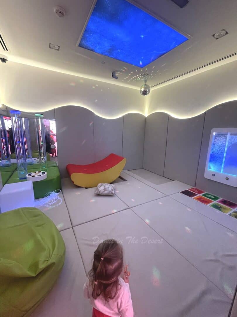 A white play room with led lighting with a bean bag chair and interactive displays for young children at Dubai Police station 