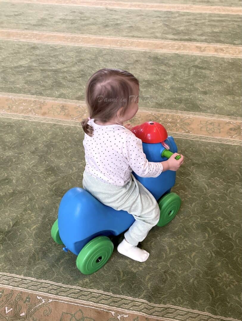 A small toddler on a blue push-along riding toy on the carpets of Jumeirah mosque in Dubai