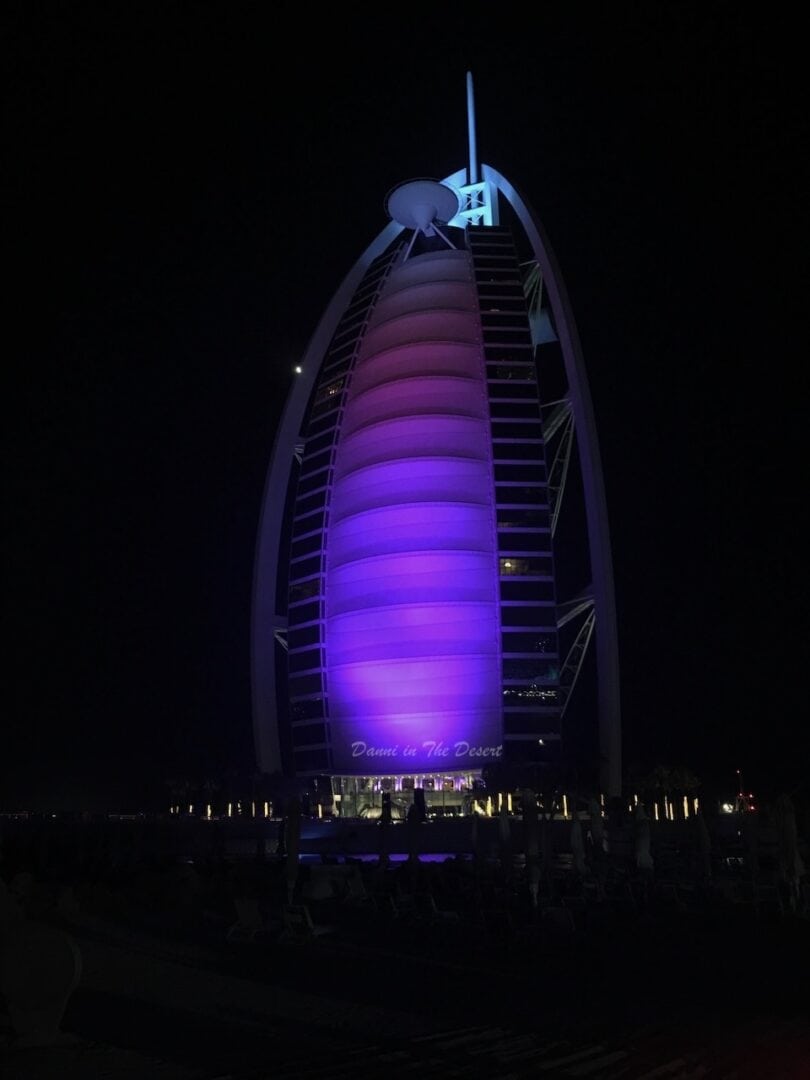 Burj Al Arab lit up purple at night time with a fully black sky in the background