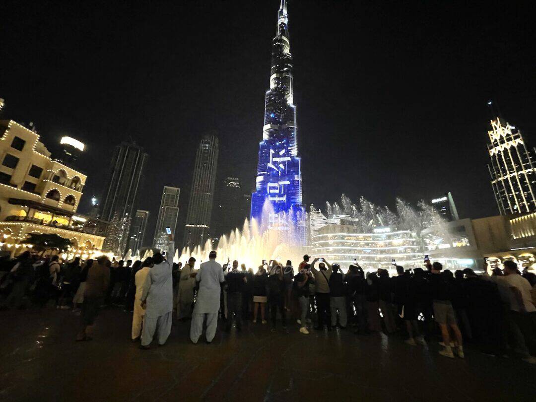 Crowds gathering to watch Dubai Fountain at night from the Dubai Mall Promenade with Souk Al Bahar, Burj Khalifa and the Downtown Dubai skyline in the background