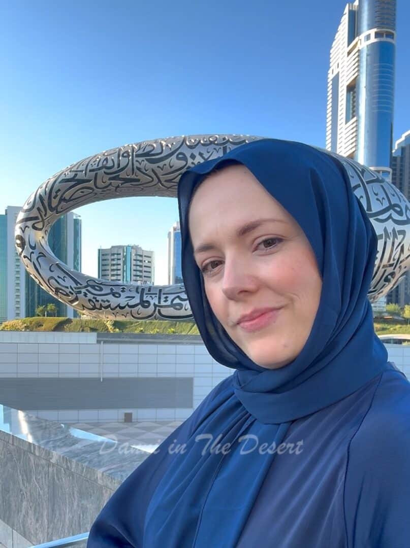 Danni B from Danni in The Desert wearing a blue abaya in front of Museum of the Future with the iconic building in the bakcground with Arabic calligraphy written all over it