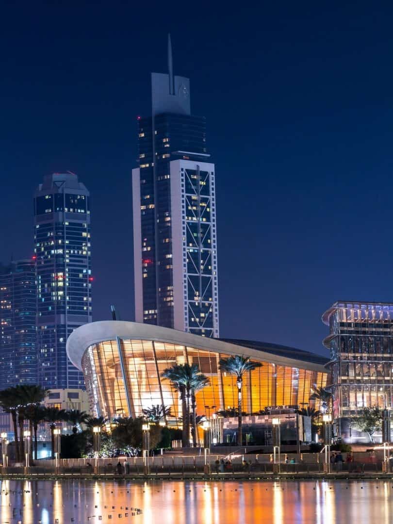 Dubai opera house lit up at night, overlooking Burj Lake with it's famous curved roof that is inspired by a dhow boat with other downtown dubai skycrapers in the background