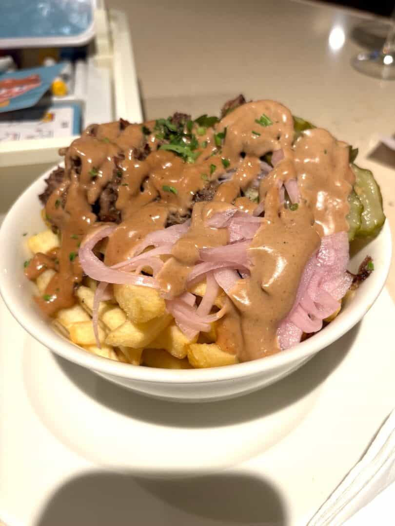 Brisket loaded fries in a white bowl with sauce dribbled all over and toppings from Mattar in Time Out Market