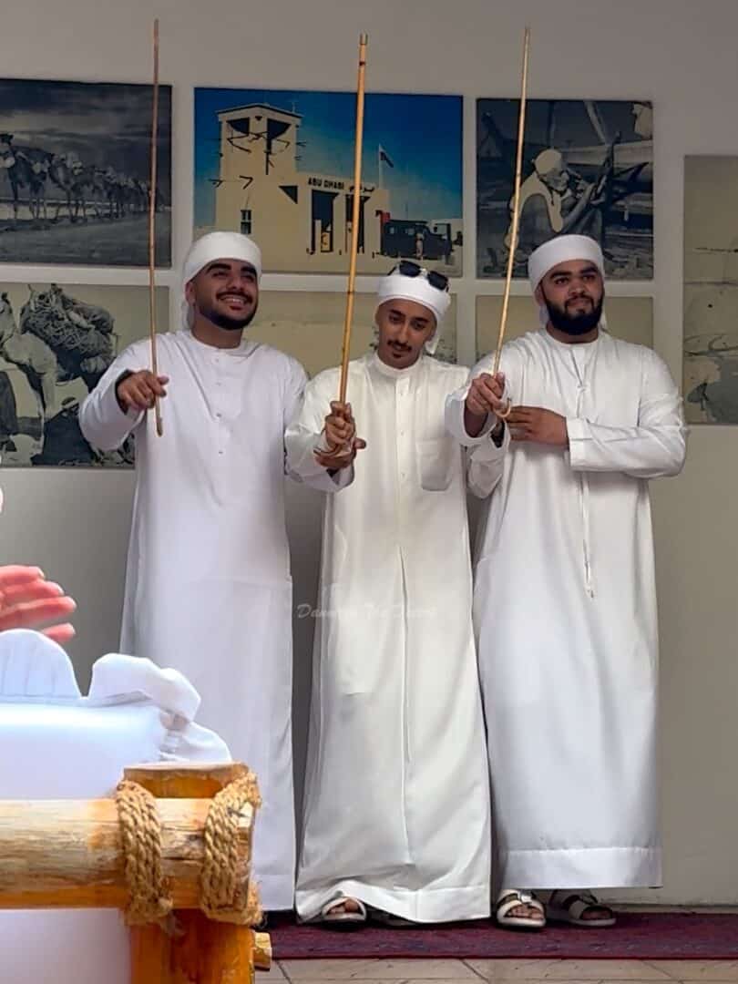 Three Emirati men in traditional Emirati dress with long white kandoras, raising their thin bamboo canes for the traditional dance performed in an Emirati restaurant